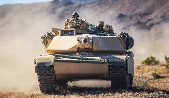 M1 Abrams tank and crew moving through dust during maneuvers