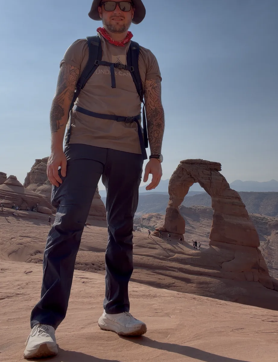 Brison McPhail standing on the slickrock with Delicate Arch behind him