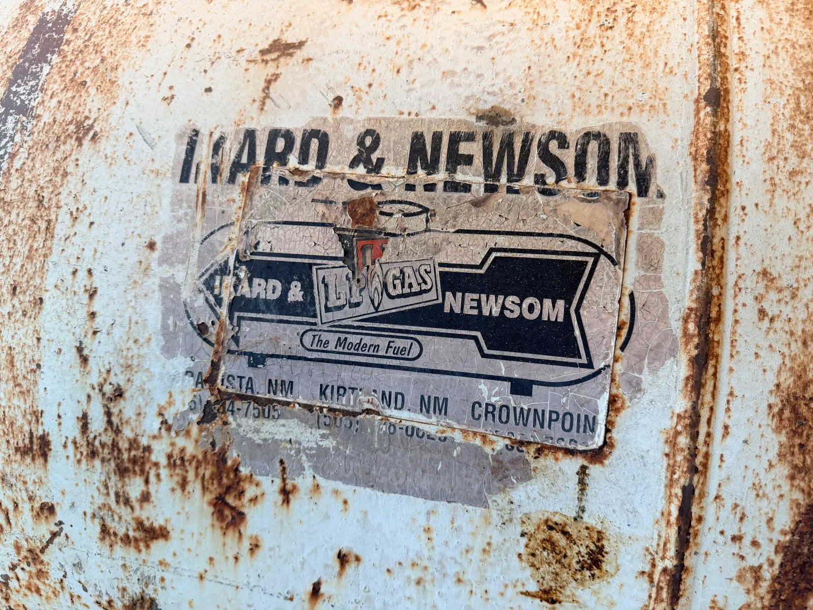 The Ward & Newsom LP Gas 'The Modern Fuel' lettering ghosting through rust on a 1,000-gallon propane tank turned smoker