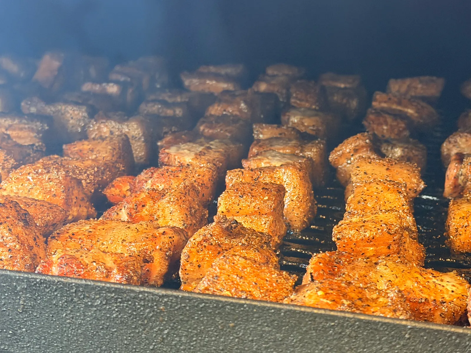 Rows of peppered pork belly burnt ends on the smoker grates at Wright's Barbecue in Benton