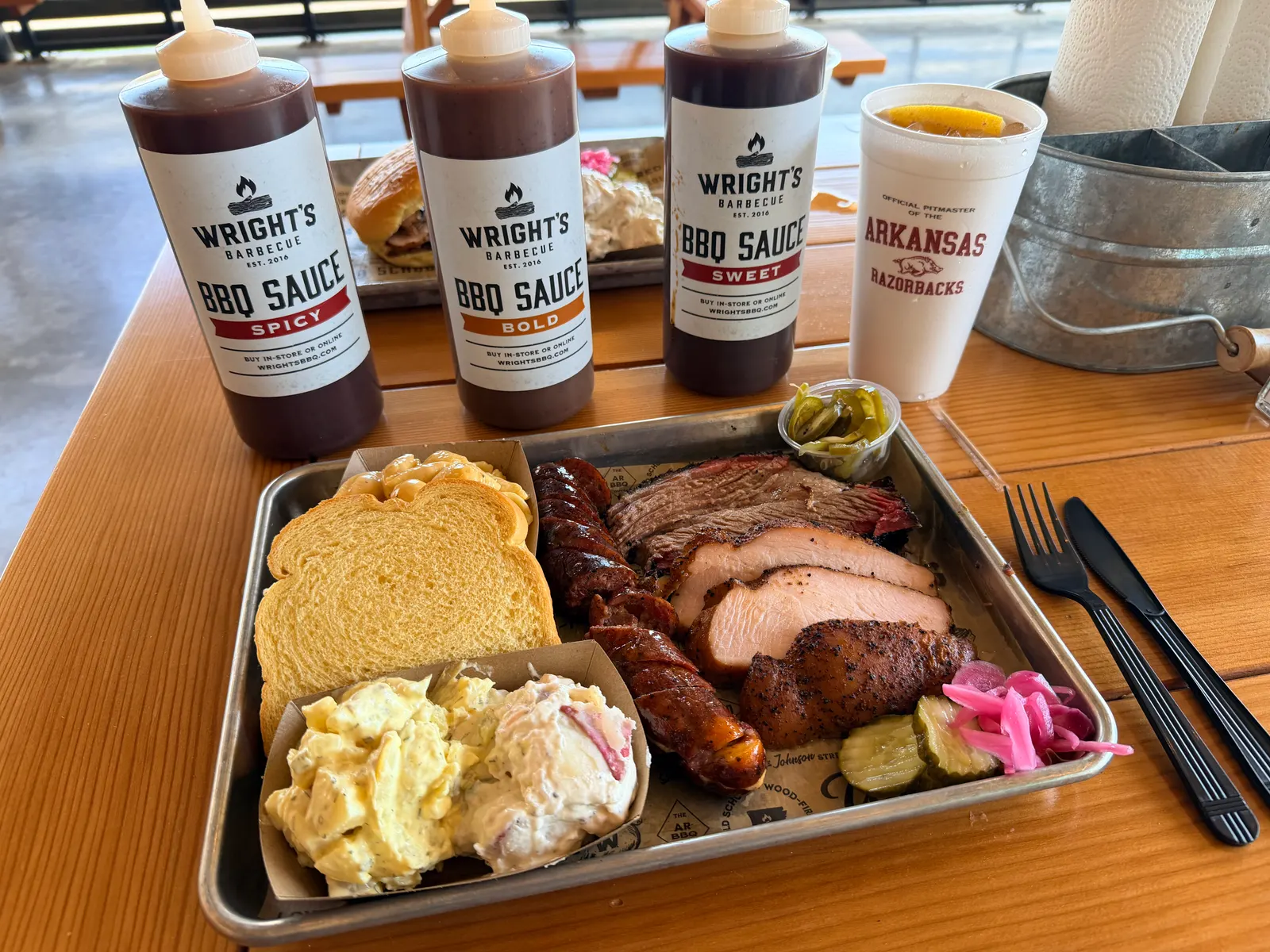 Wright's Barbecue sauce bottles — Spicy, Bold, and Sweet — beside an Official Pitmaster of the Arkansas Razorbacks cup and a loaded tray