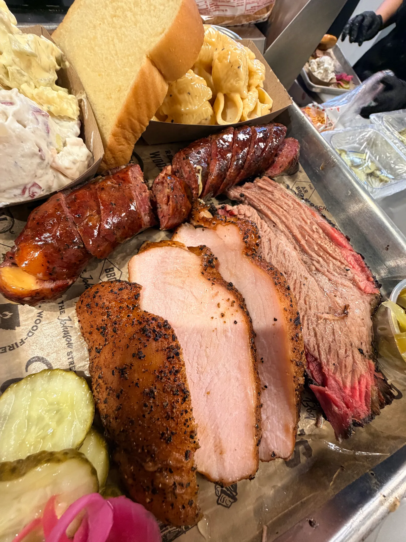 A loaded Wright's Barbecue tray with sliced brisket, peppered smoked turkey, cheese-stuffed sausage, shells and cheese, potato salad, bread, pickles, pickled onions, and jalapeños